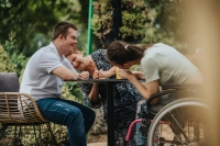 A group of friends, including a boy with Down syndrome and a girl in a wheelchair, share a laugh outdoors, highlighting friendship and inclusivity.